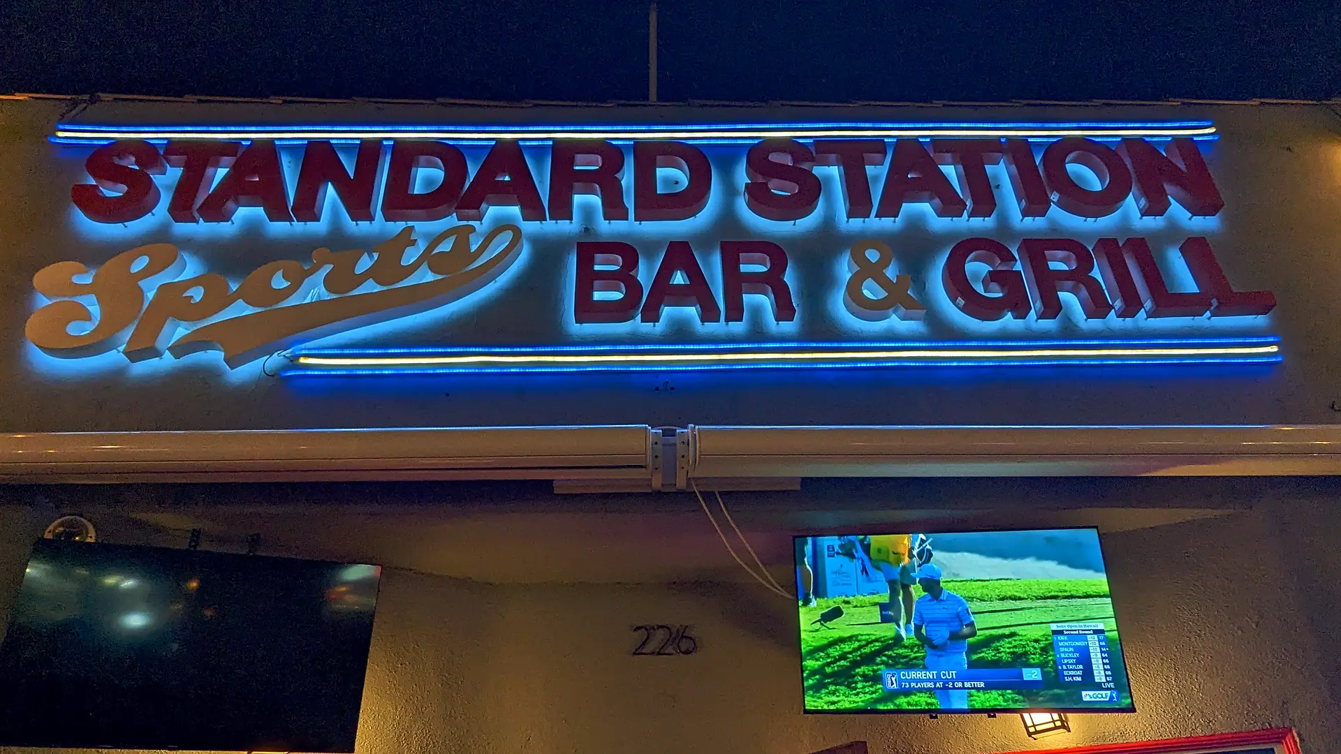 The Standard Station sign lit at night, red letters and blue neon over the front of the building, house number 226 on the wall