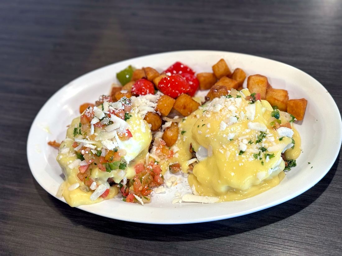 Eggs Benedict covered in hollandaise with pico de gallo, cotija, and home fries on a white plate