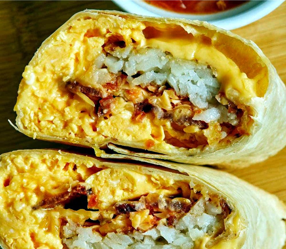 A breakfast burrito cut in half, showing egg, cheese, bacon, and hash browns inside