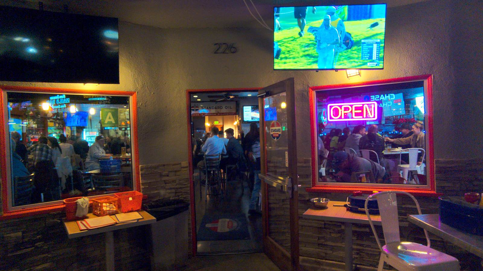 The front door of Standard Station at night, standing open with an OPEN neon sign in the window and the crowd glowing inside