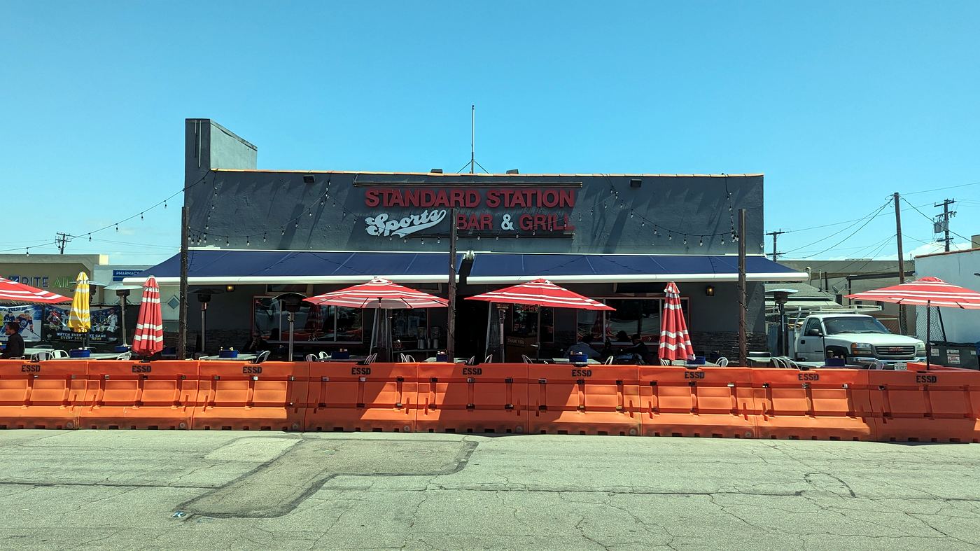 Standard Station by day: the full facade with its sign, patio tables, and red and white umbrellas