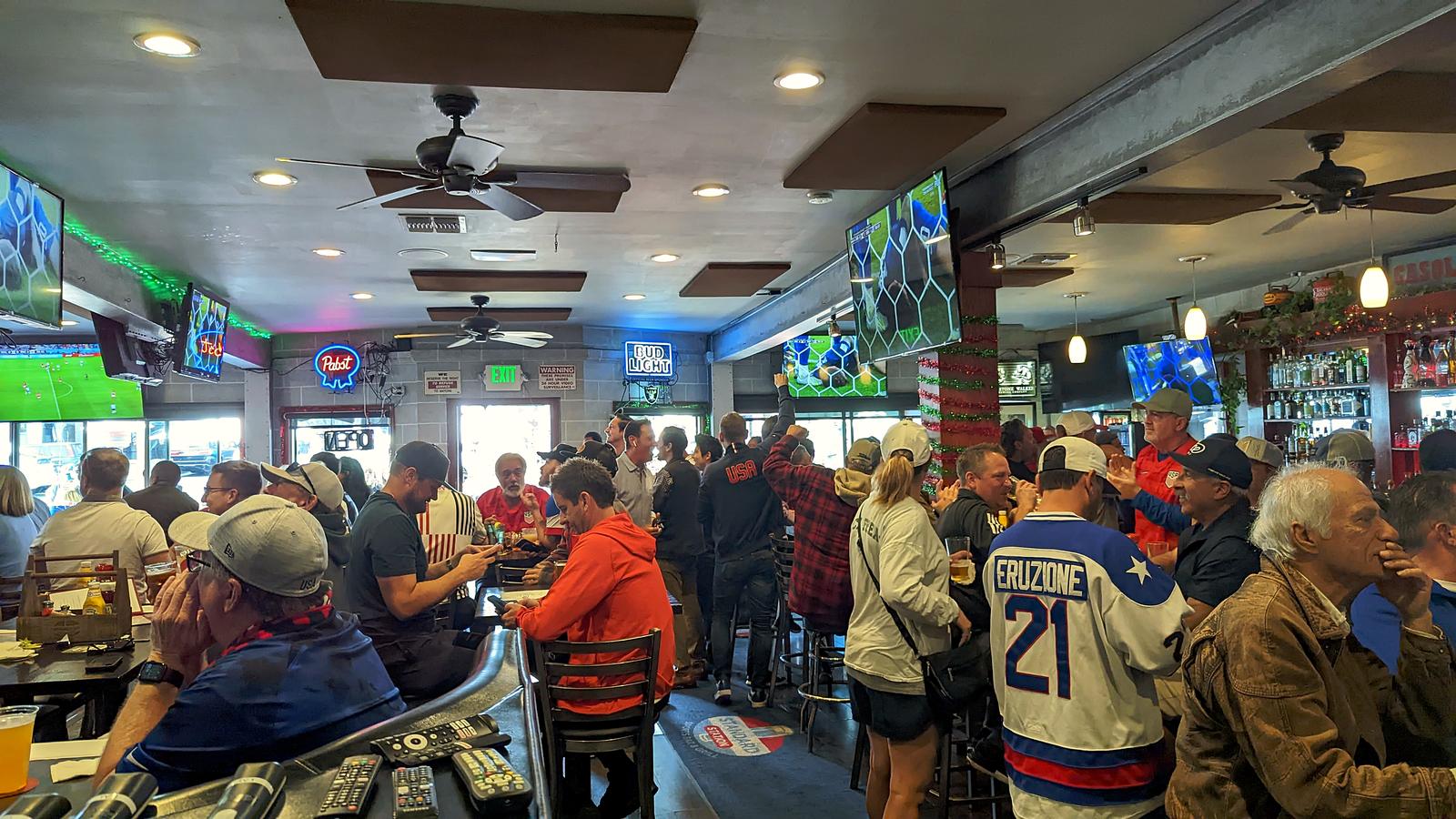 A packed World Cup crowd at Standard Station, fans in USA shirts watching the match on the wall screens
