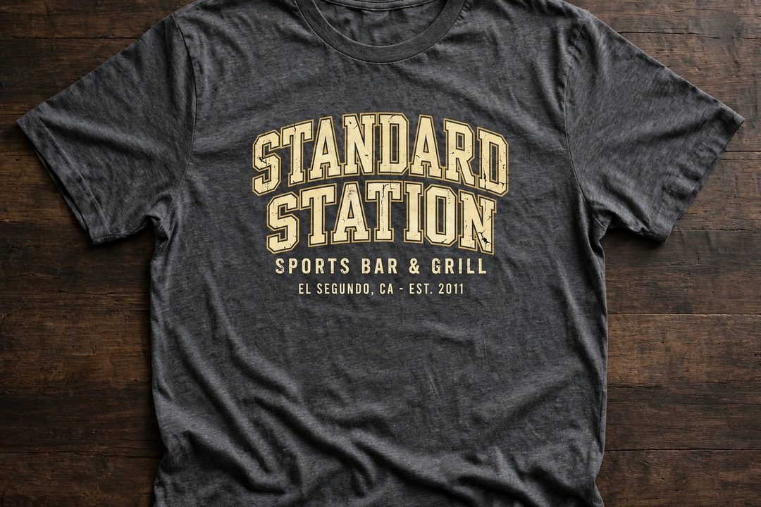AI-built merch concept for Standard Station: a charcoal tee with the venue name in arched collegiate letters over Sports Bar and Grill, El Segundo, California