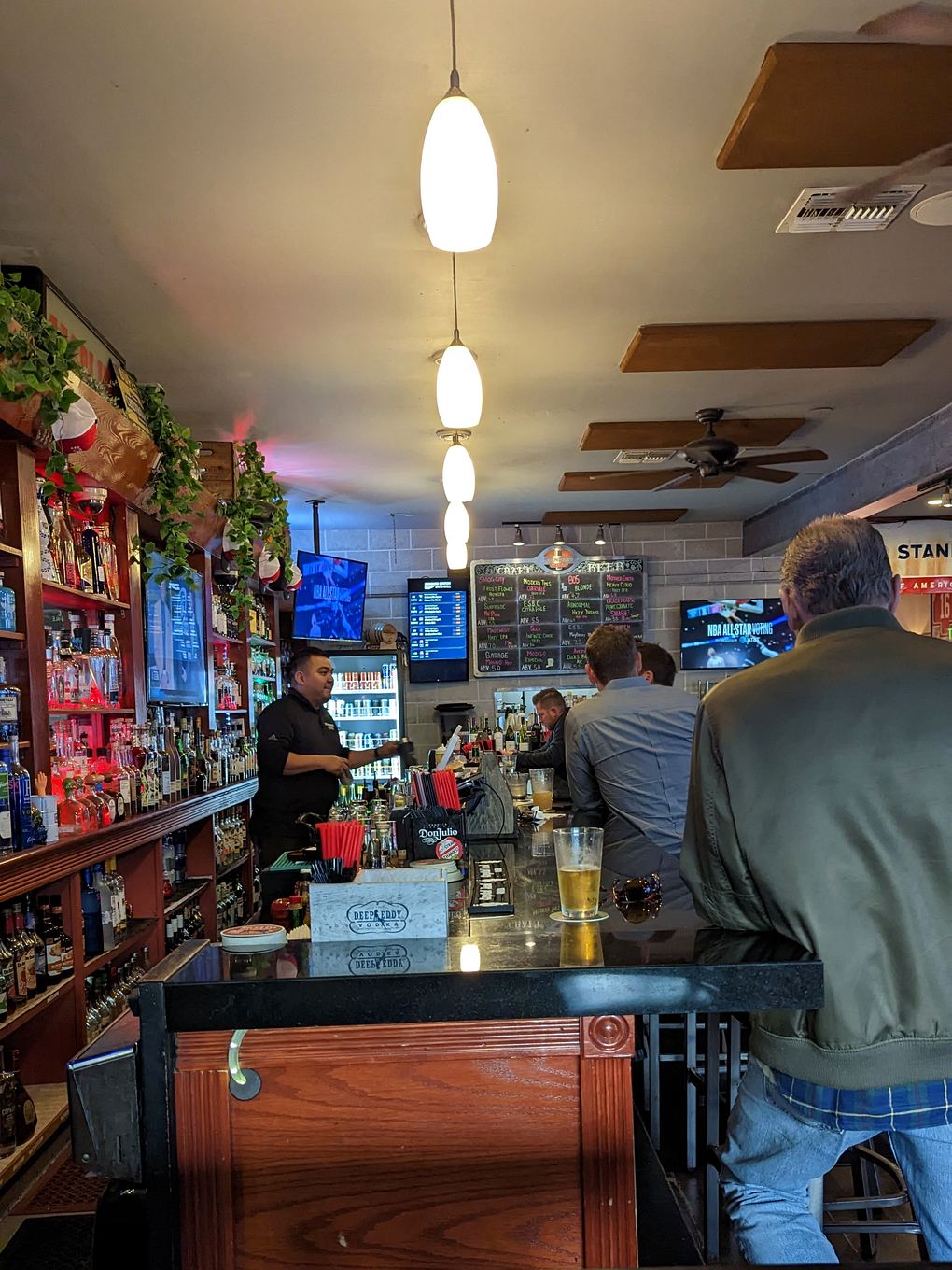 Looking down the bar rail at Standard Station, a beer on the counter, the bartender working, the draft board on the back wall