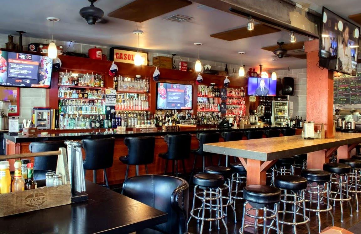 The bar at Standard Station in a quiet moment, stools lined up under warm light and lit shelves