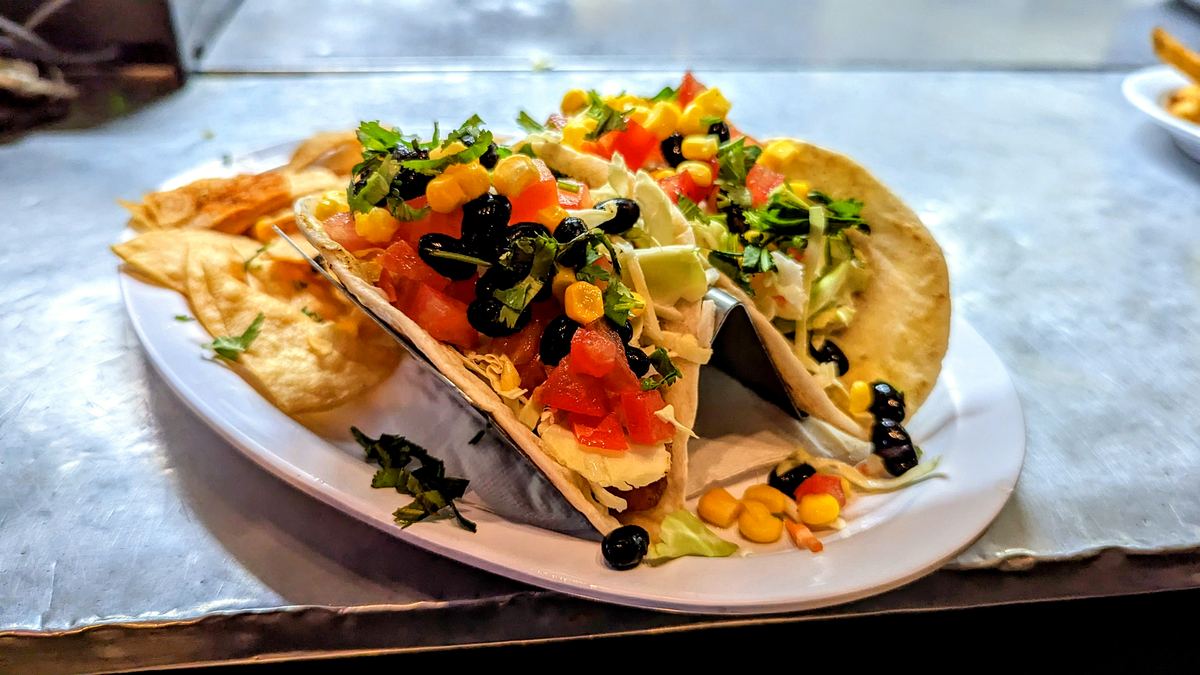 Two tacos topped with black beans, corn, cabbage, and pico de gallo, on a plate with tortilla chips